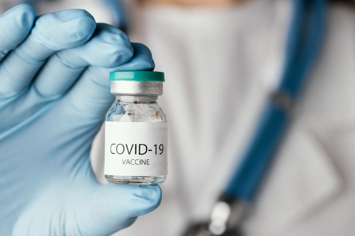 A gloved hand holding a small medical vial labelled COVID-19