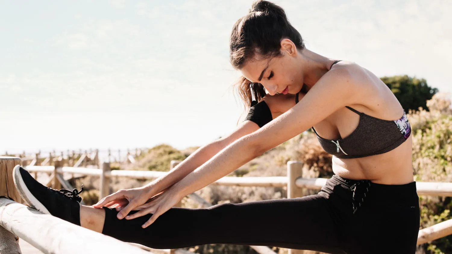 A woman stretching a raised leg against a boardwalk rail