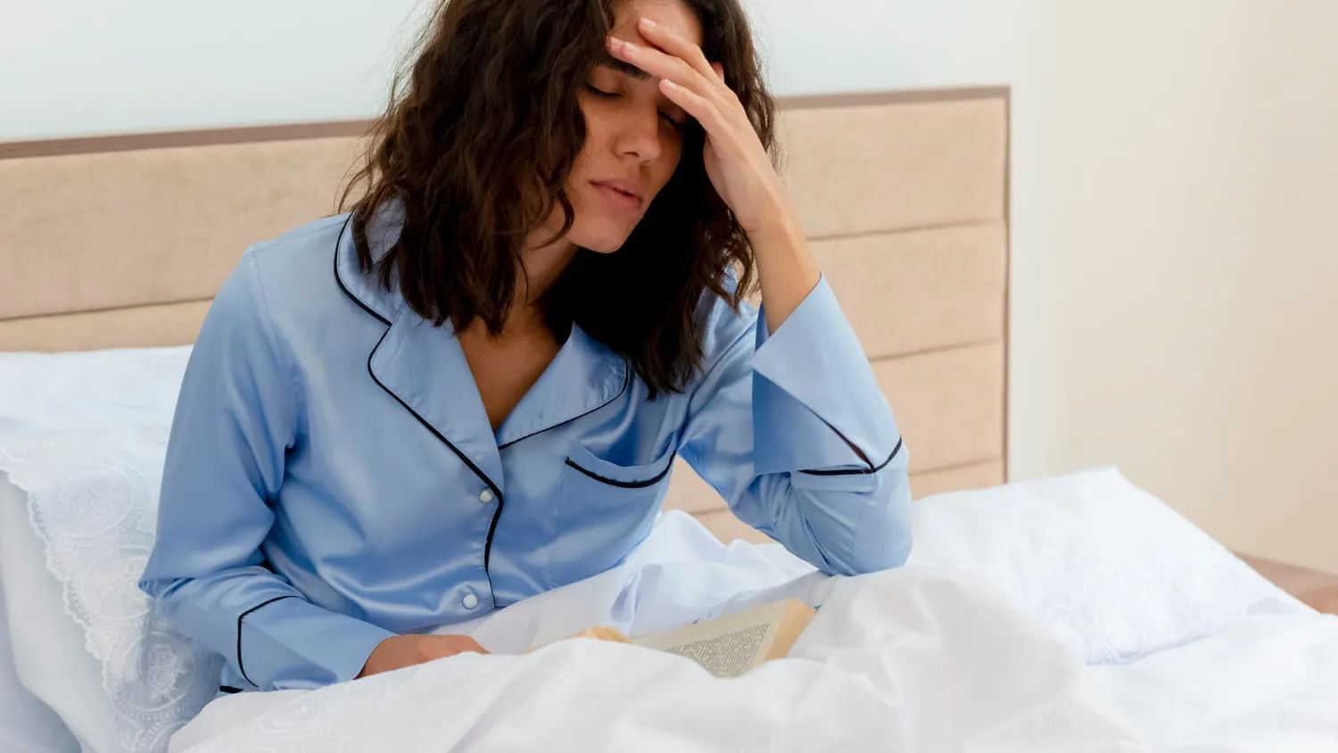 A woman sitting up in bed in pyjamas with a hand to her forehead