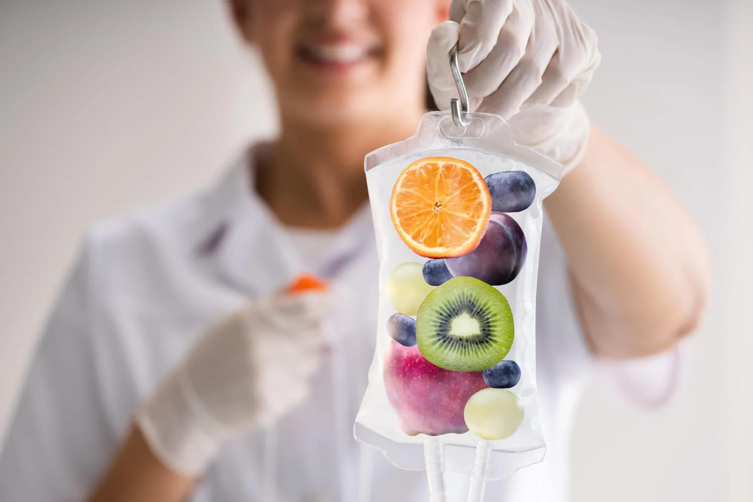 A gloved clinician holding up an IV bag illustrated with slices of orange, kiwi, apple and grapes