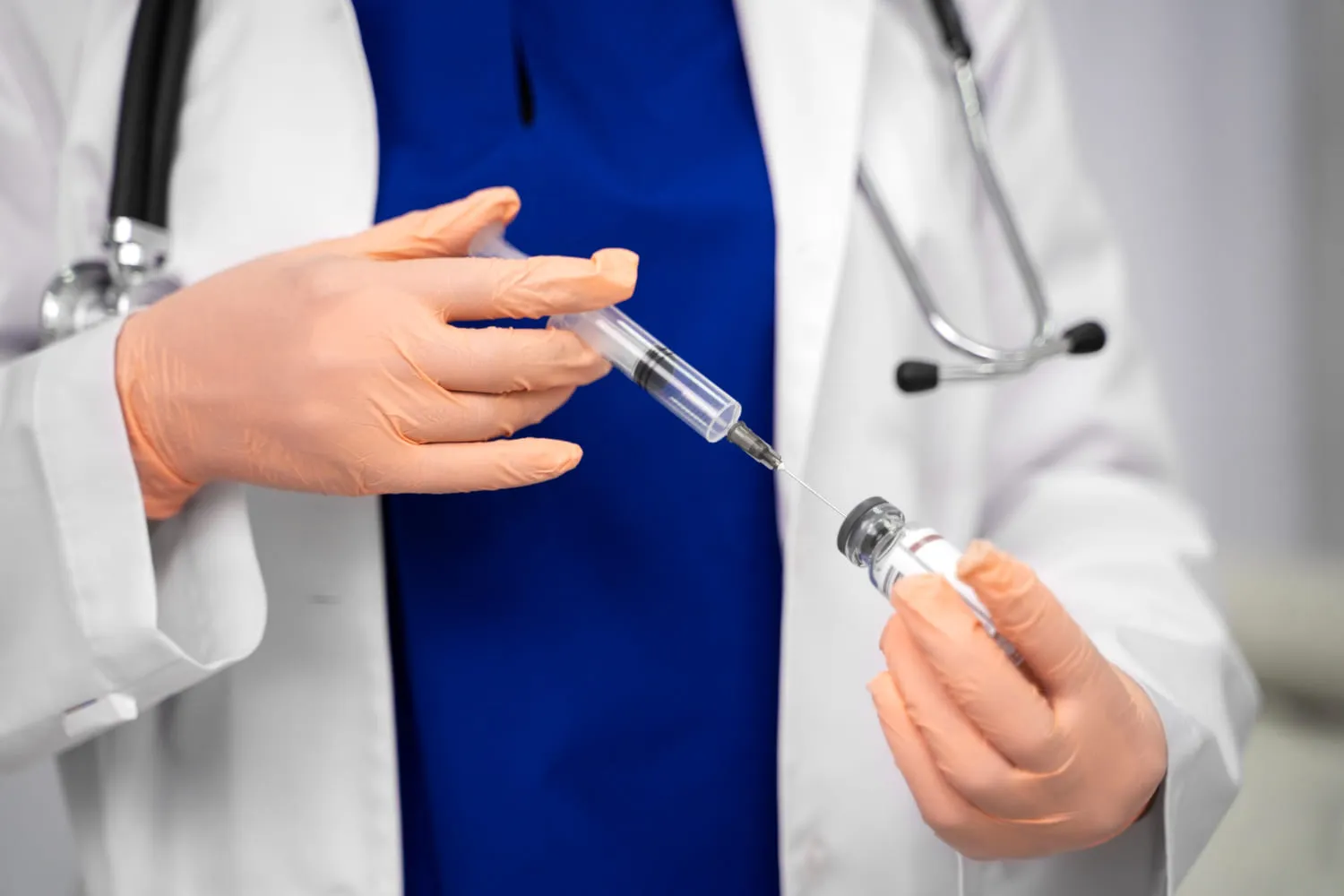 A clinician drawing a dose from a vial into a syringe