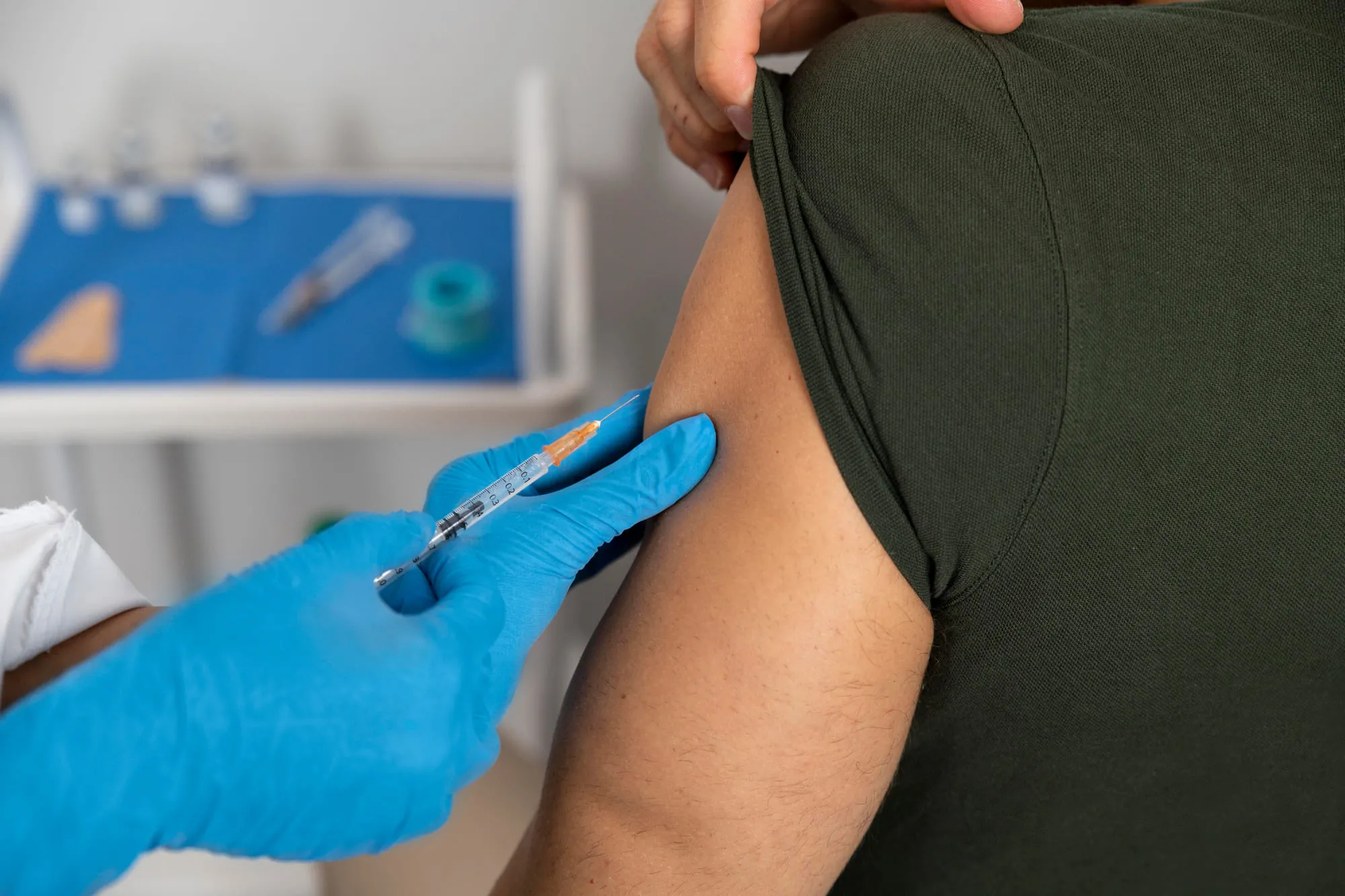 A gloved clinician giving a vaccine into a patient's upper arm