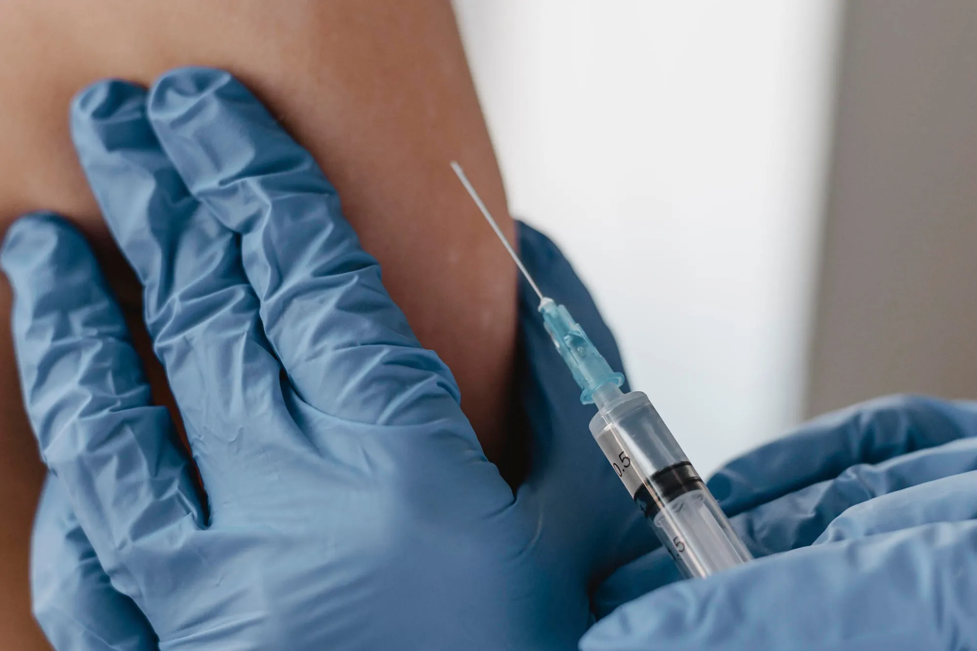 A gloved clinician giving an intramuscular injection into a patient's shoulder