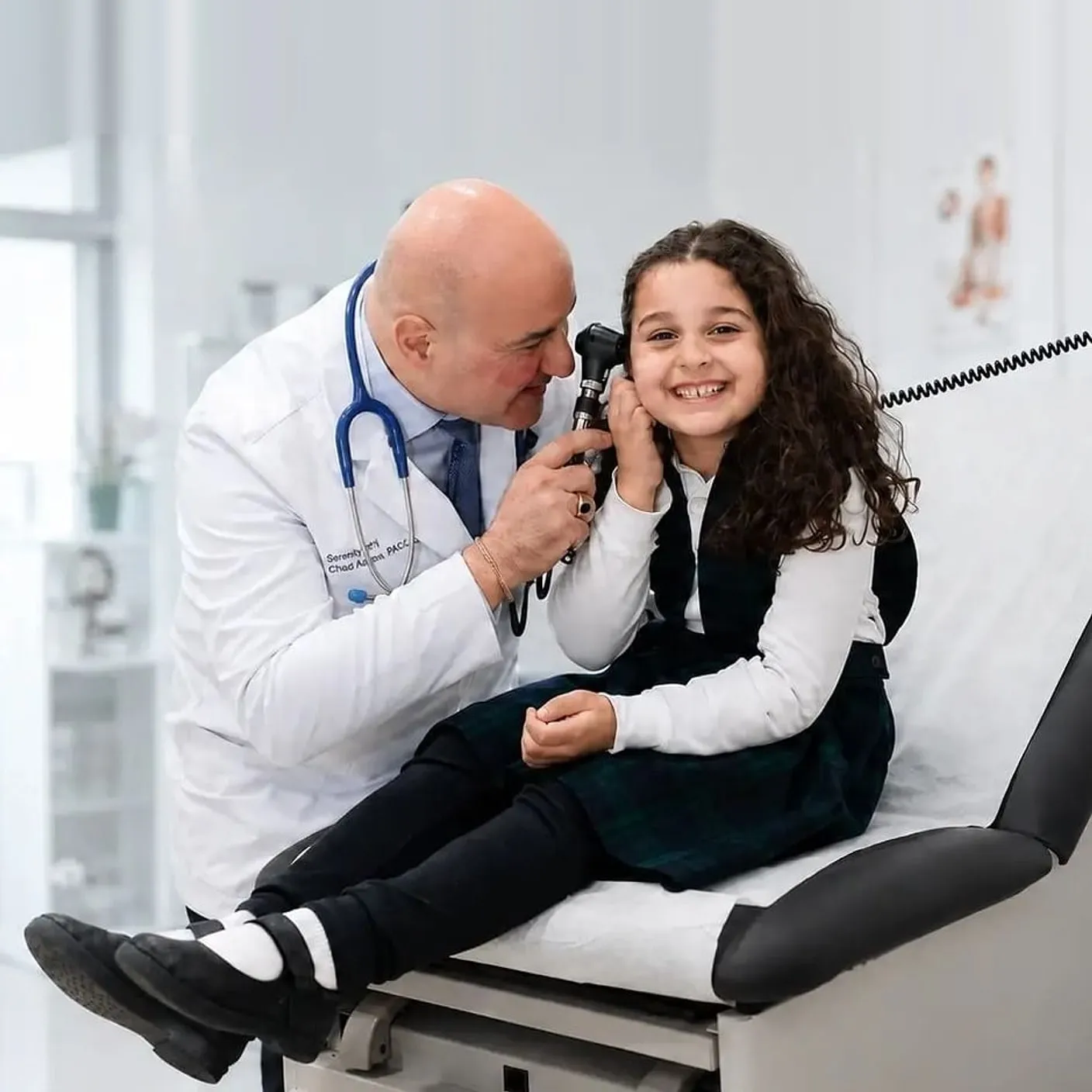 A Serenity Urgent Care provider examines a smiling young patient's ear in a bright exam room